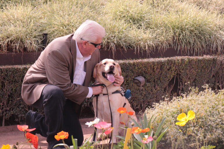 Tom Olzak leans down and smiles at his yellow Lab guide dog